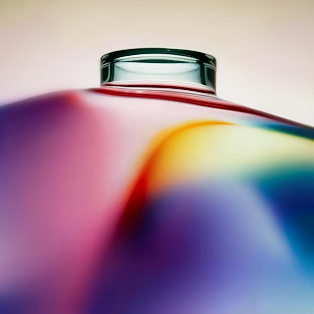A glass bottle with a rounded body and a narrow neck, with a colorful, swirly pattern on the body.
