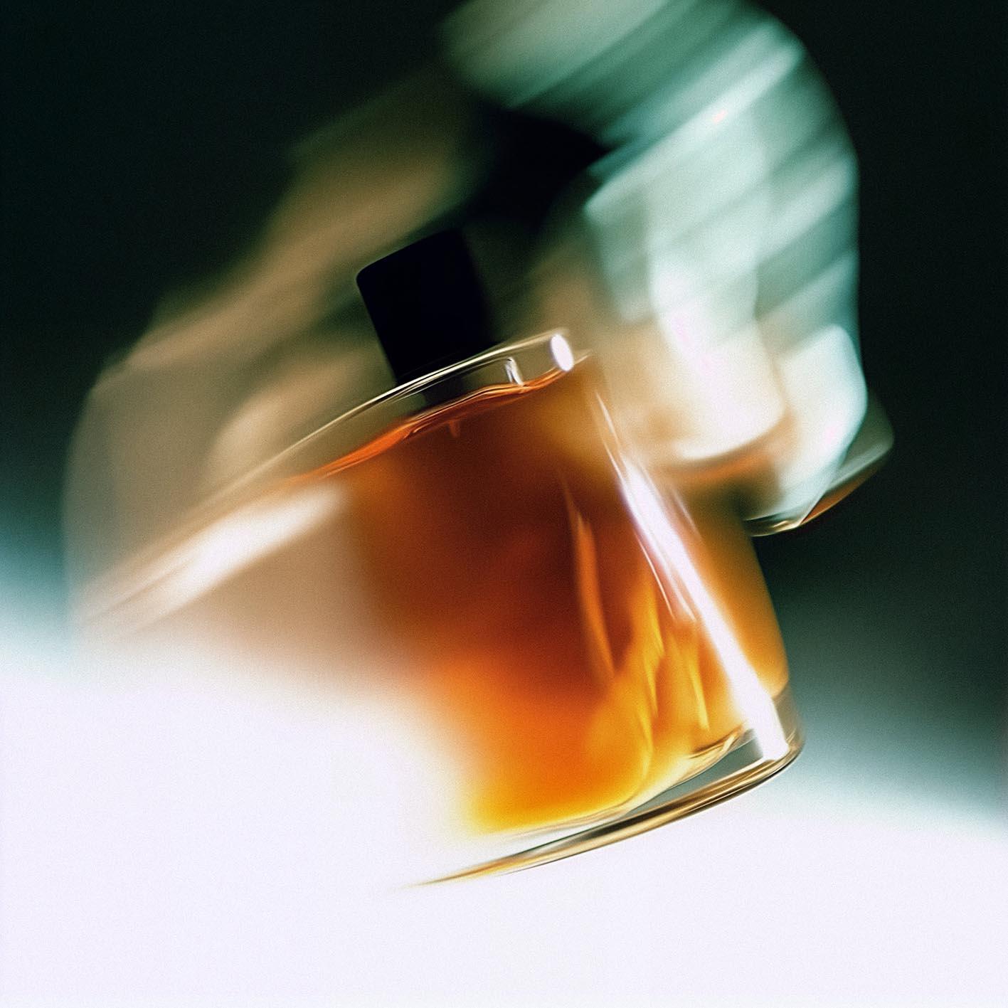 A perfume bottle with a dark glass body and a golden cap, partially filled with a golden liquid.