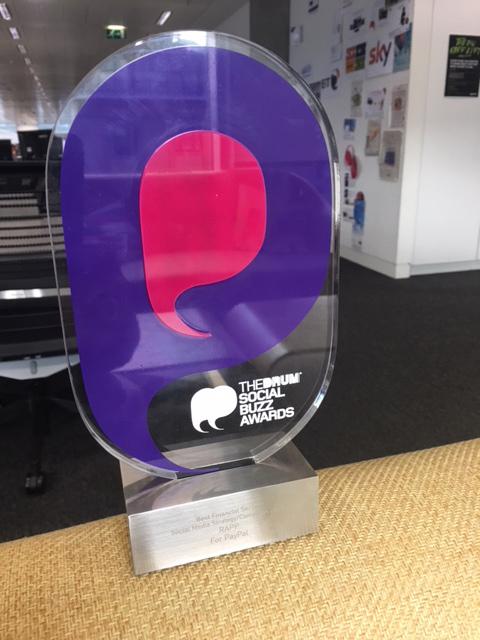 A glass award with purple and red designs featuring 'The Drum' and 'Social Buzz' awards in speech bubbles.