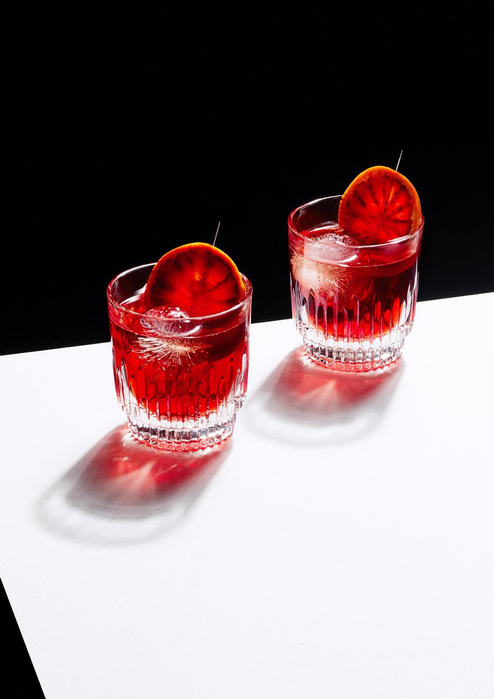 Two red Negroni cocktails in crystal glasses with an orange slice.