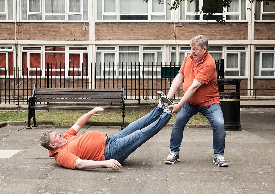 Two men engage in a physical activity in a park, with one man lying on the ground and another supporting him.