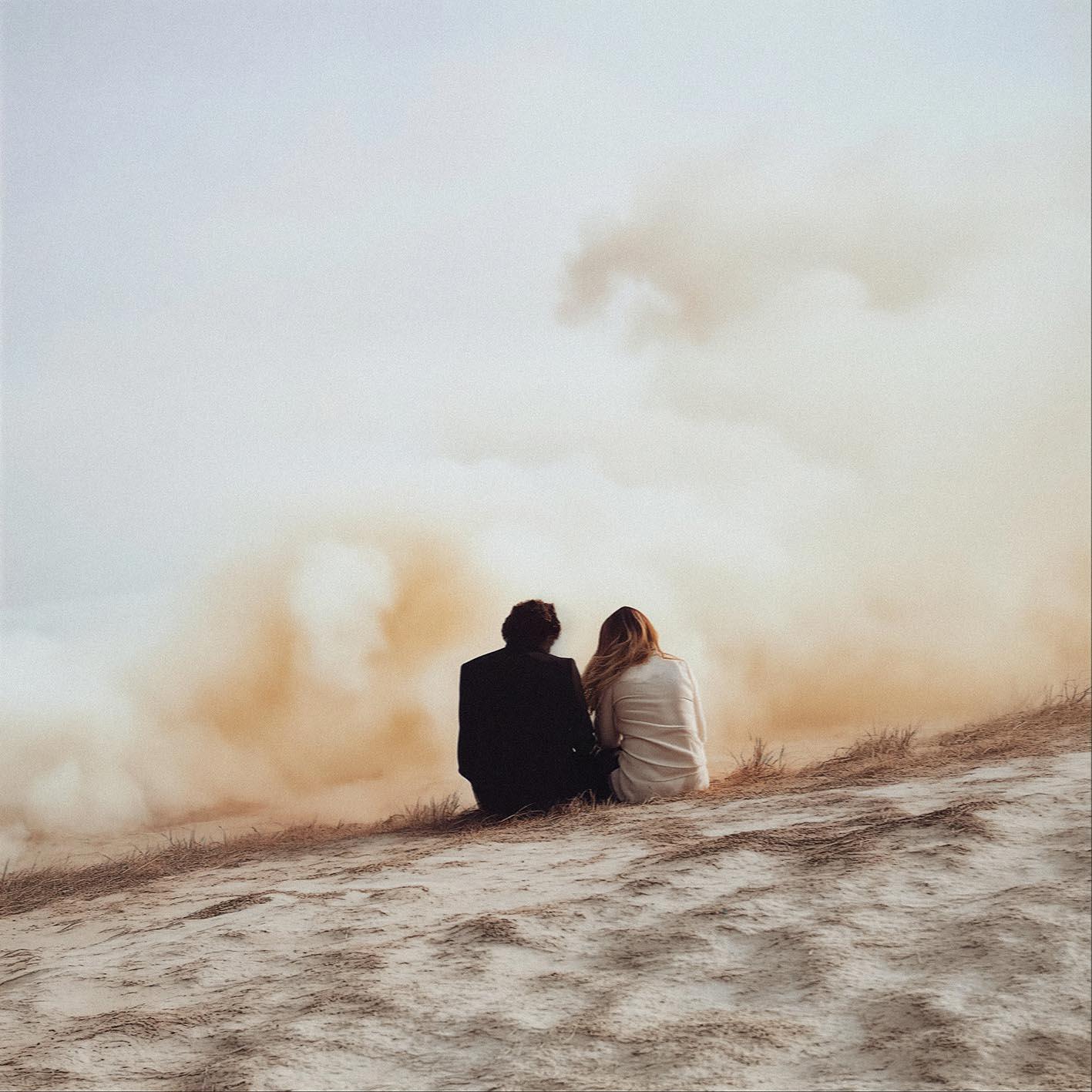 A couple sitting on a beach, watching the sunset.