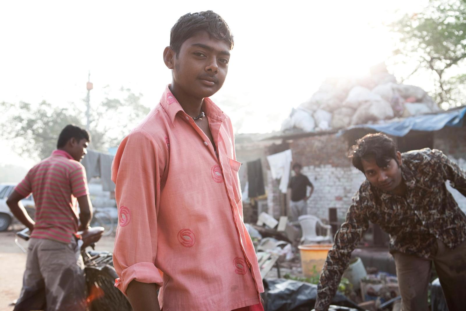A boy in a pink shirt stands among vendors and customers in a busy market.