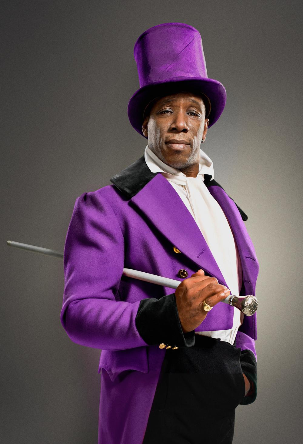 A man in a purple top hat, purple tailcoat, and white shirt, holding a silver-tipped cane.