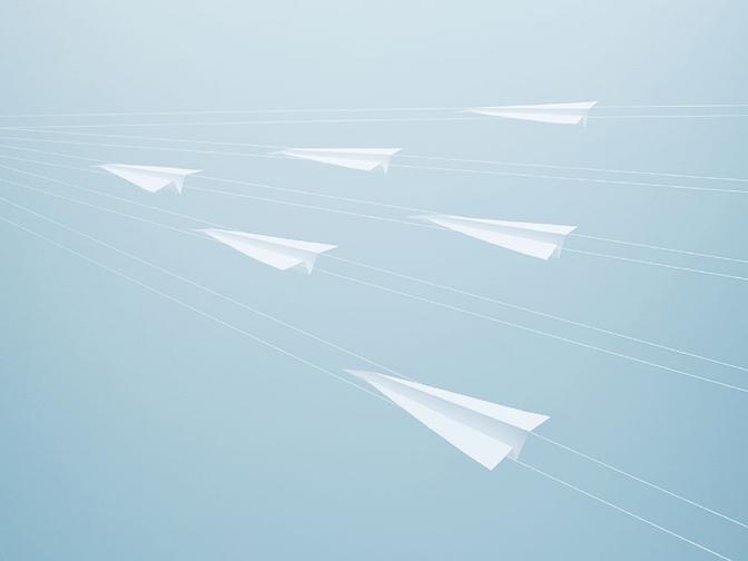 A collection of white paper airplanes in flight, suspended in mid-air against a blue sky background.