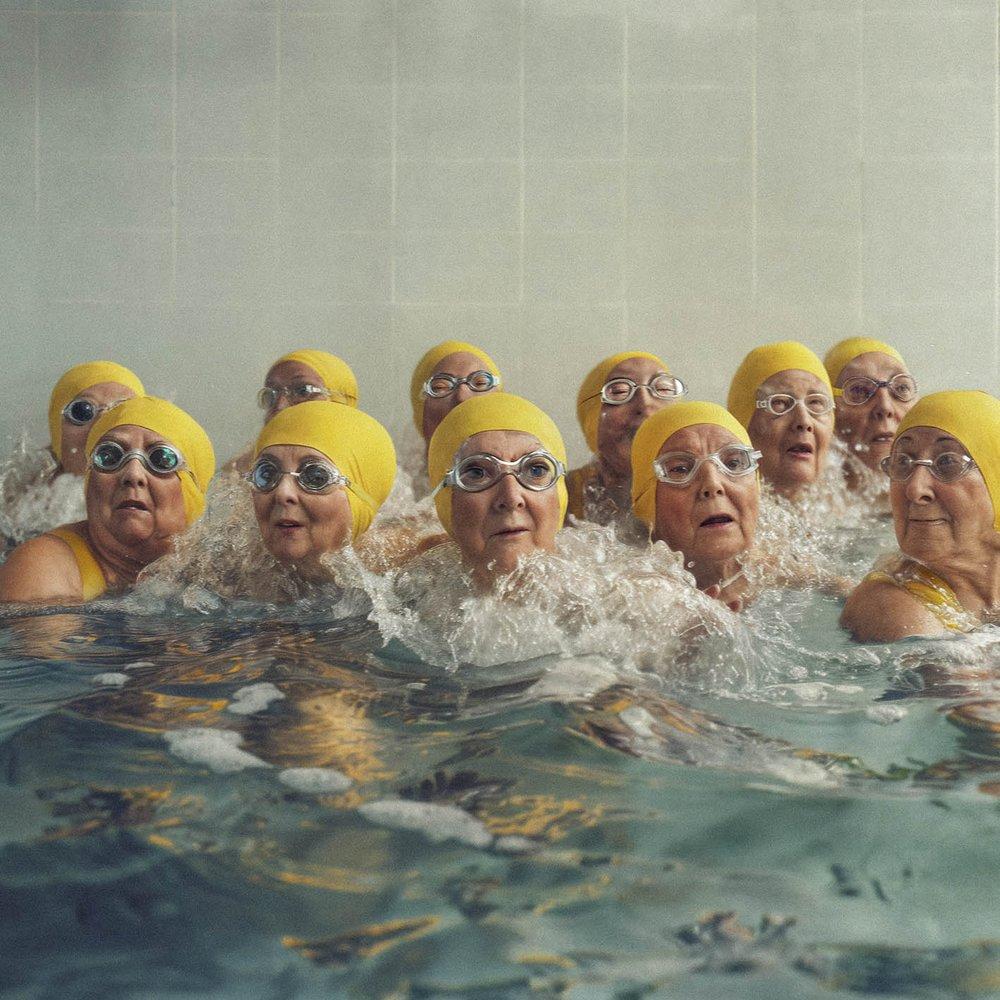 Elderly women in swimming caps and goggles, wearing swimsuits, in a swimming pool.