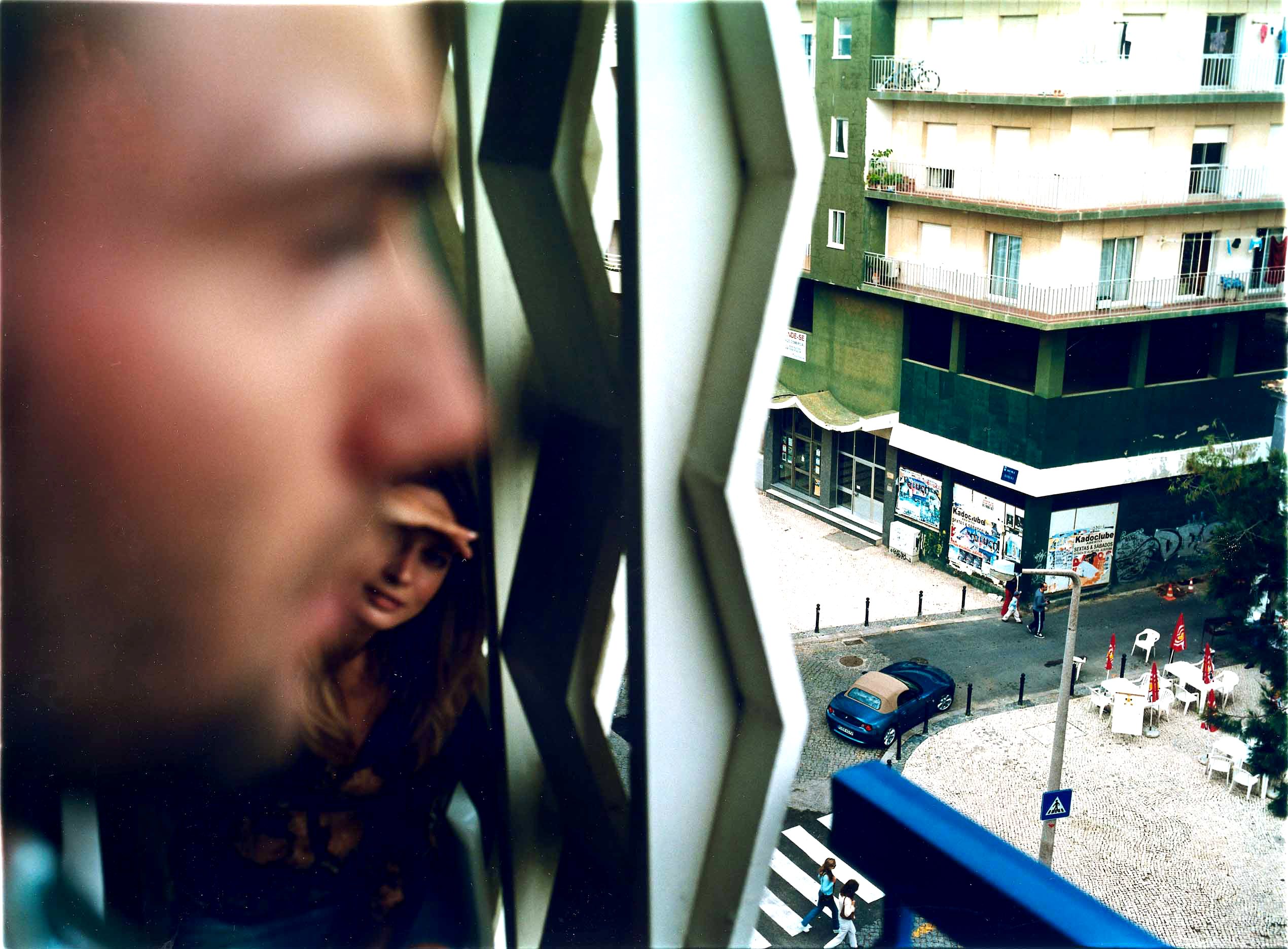 A man and a woman are peering through a window, looking out at a city street below.