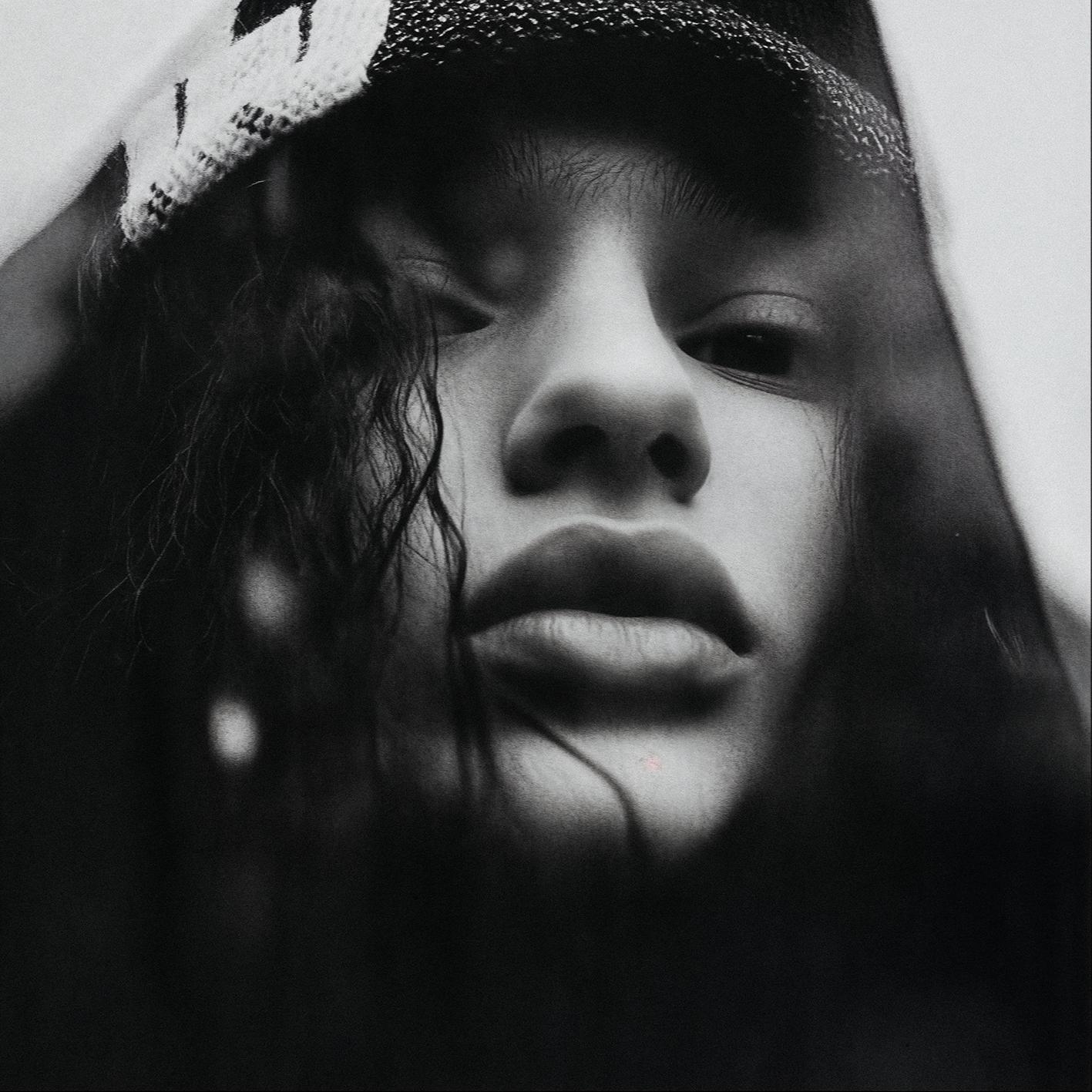 Close-up of a face with black and white, pixelated, distorted, and glitchy effects, featuring a white, pixelated 'A' logo on the forehead, wearing a black hoodie.