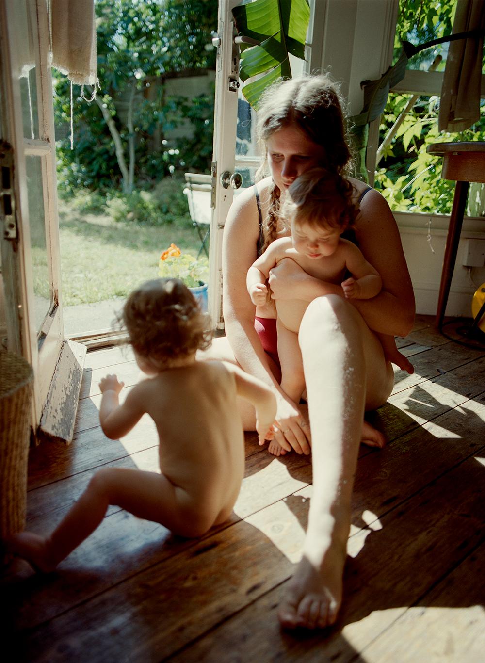 A woman sits on the floor with two infants.