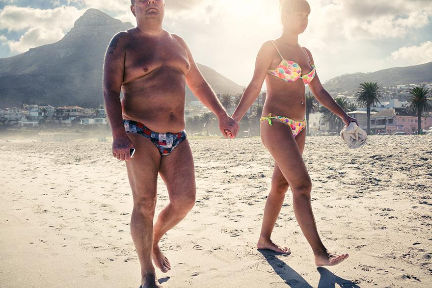 A man and a woman, both wearing swimwear, walking hand in hand on a beach.