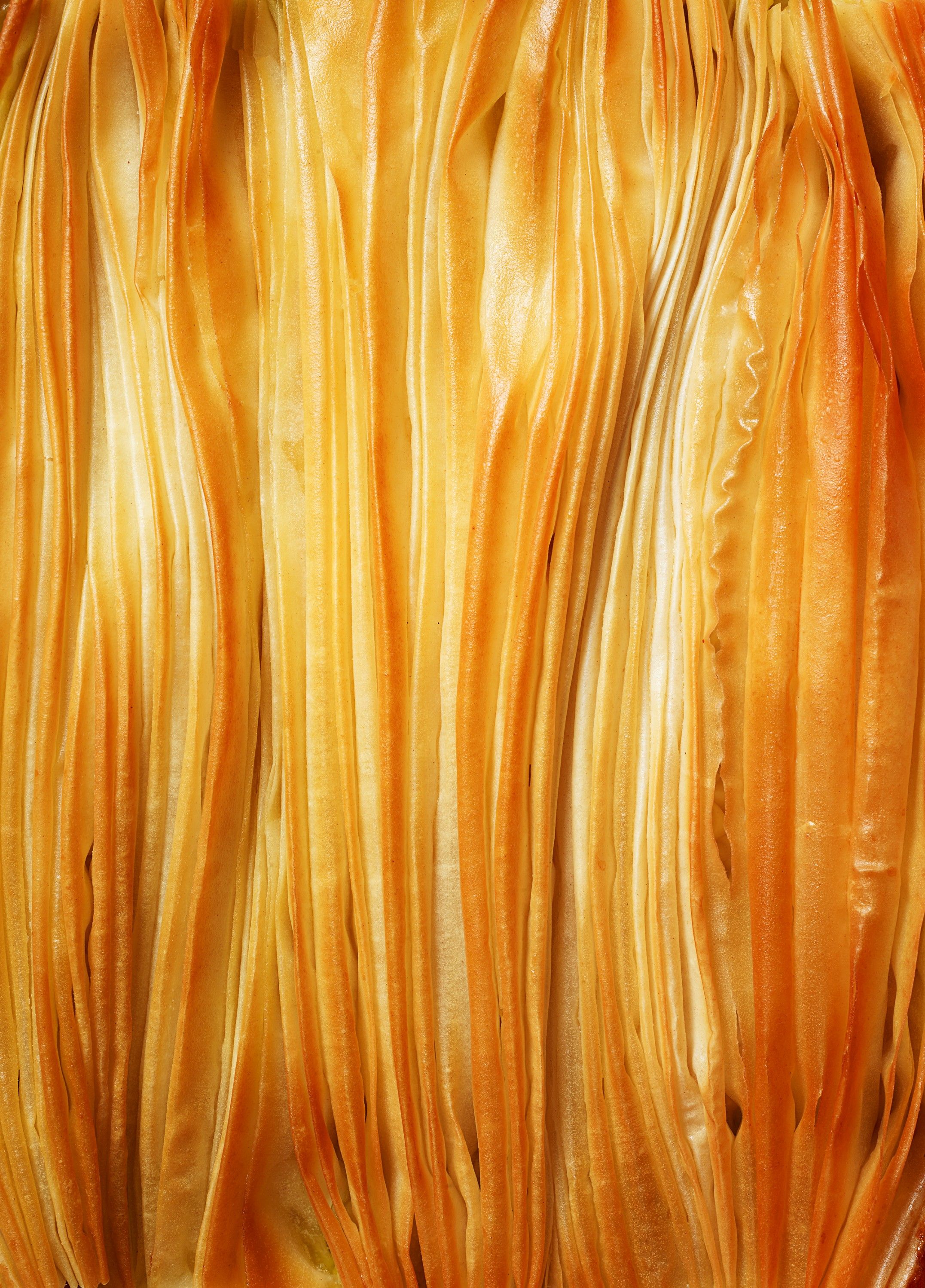 A close-up of a large, yellow, wavy, curly, fried noodle-like food item, possibly a type of Asian noodle or a specific type of fried noodle.