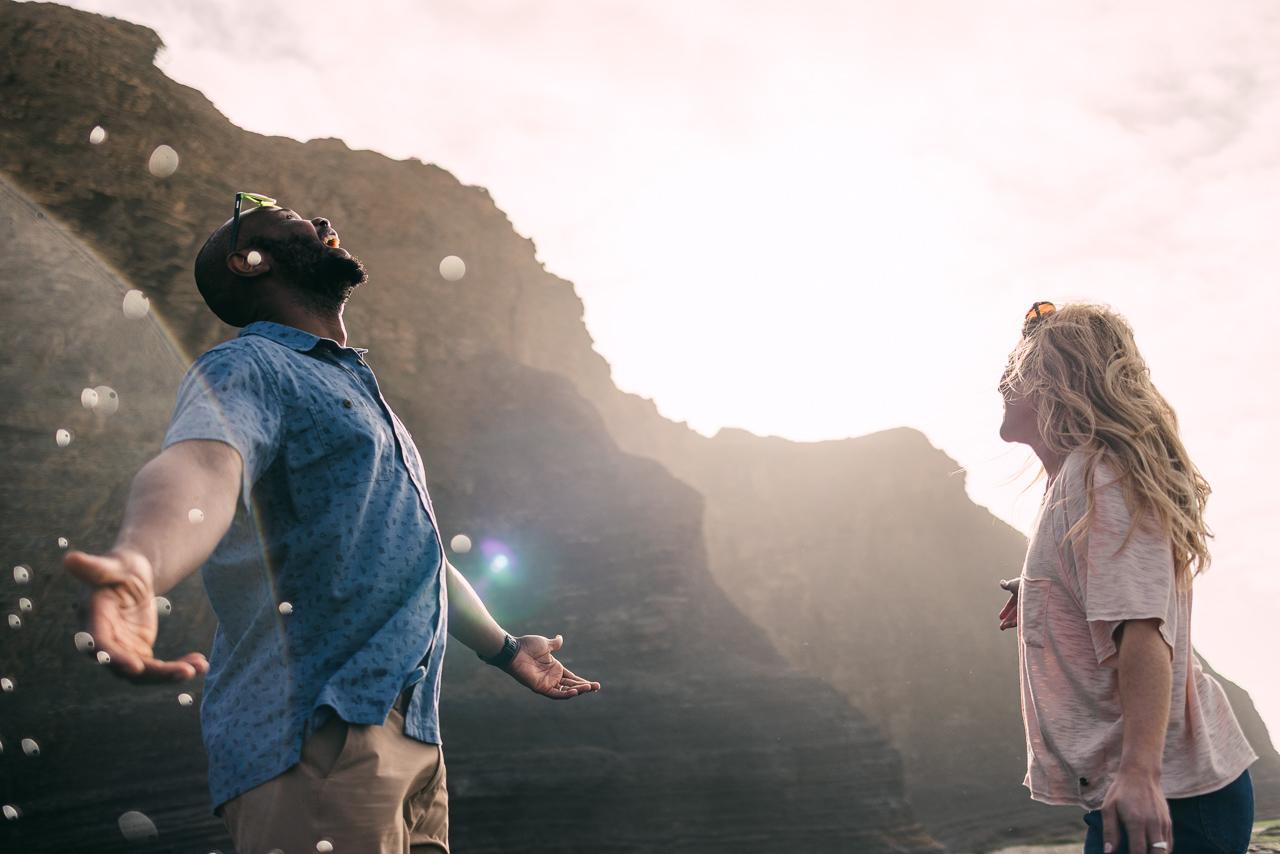 A man and woman standing on a rocky outcropping overlooking a vast landscape.