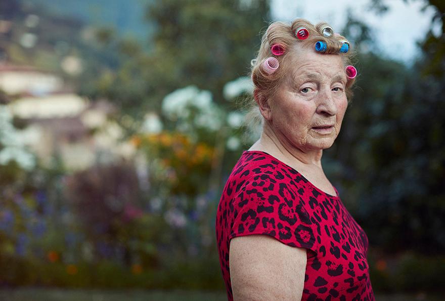 An elderly woman wears a red and black leopard-print dress with 1950s-style hair rollers.