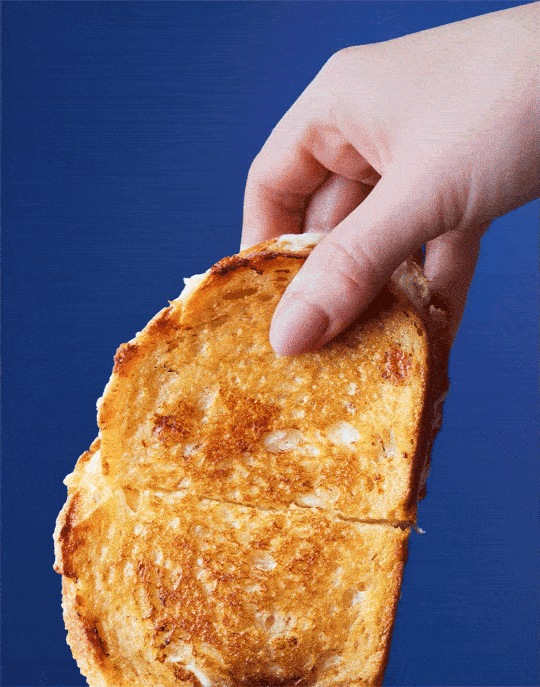 A hand holding a toasted sandwich, with the top slice being lifted to reveal the filling.