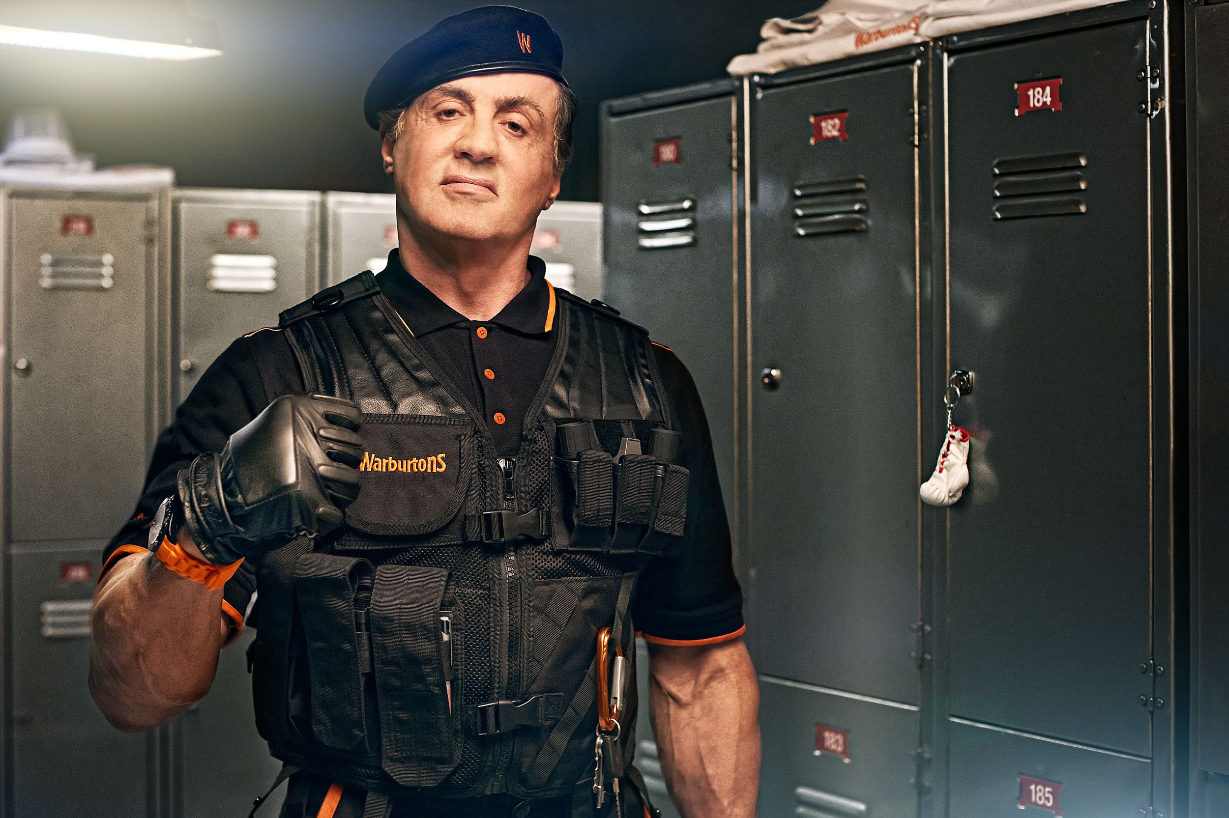 A man in a black and orange uniform with a black beret stands in front of metal lockers.