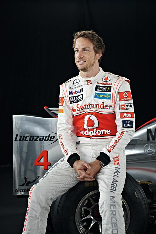 A man in a white and red racing suit sitting in front of a car.