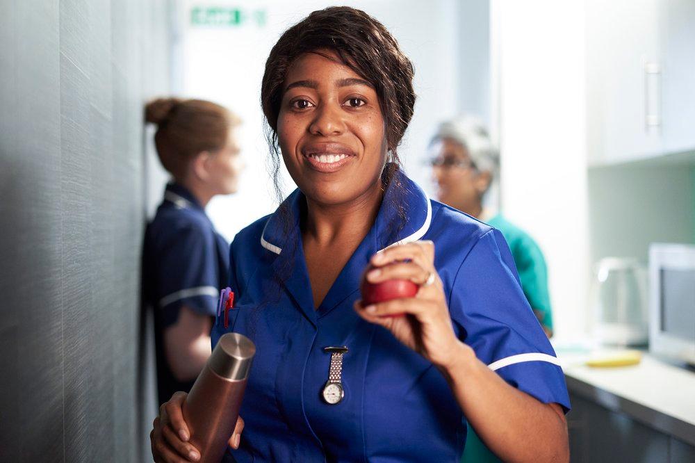 A woman in a blue nurse's uniform, holding a water bottle and a stress ball, in a hospital setting.