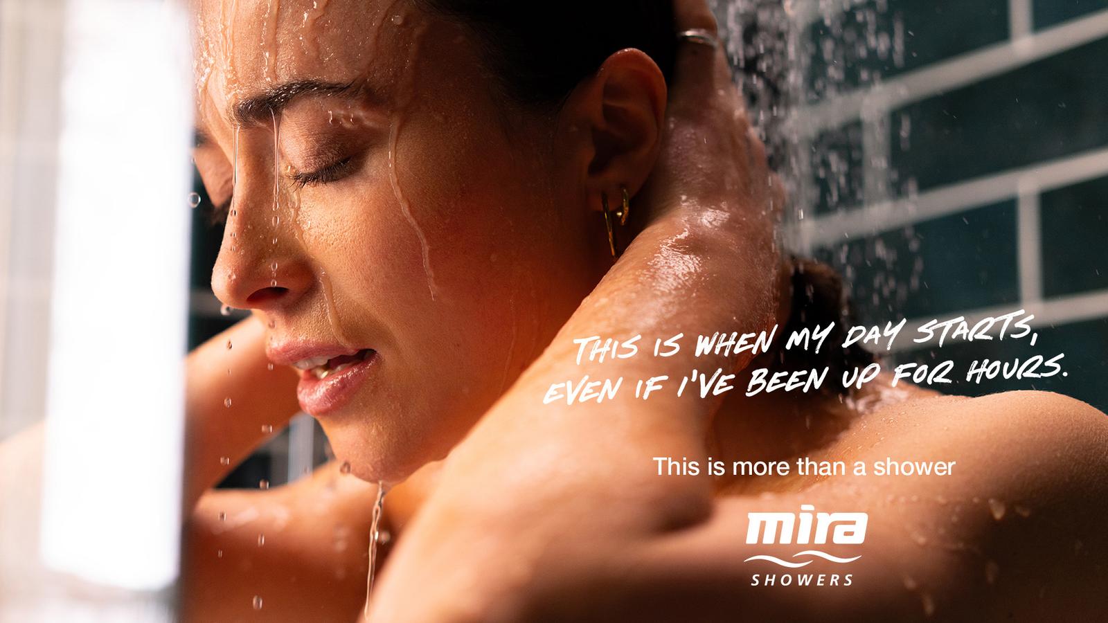 A woman in a shower with water running down her face and body, holding a quote card.