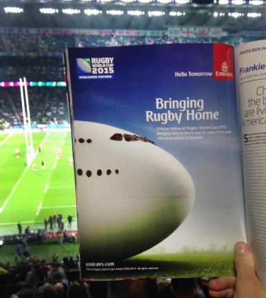 A rugby ball on a green grassy field with a stadium in the background.