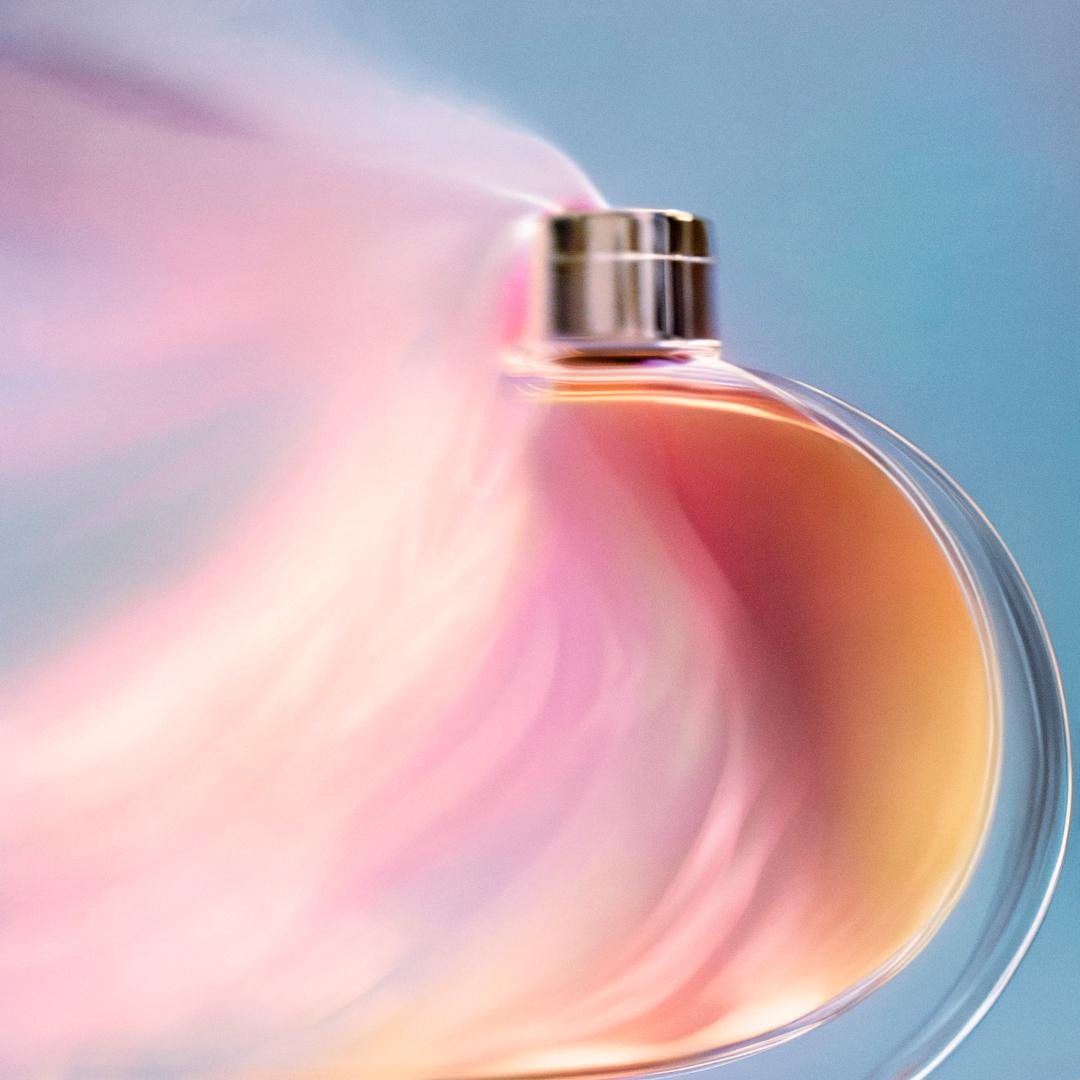 A perfume bottle with a swirling, iridescent liquid inside, emitting a misty, pinkish-violet vapor.
