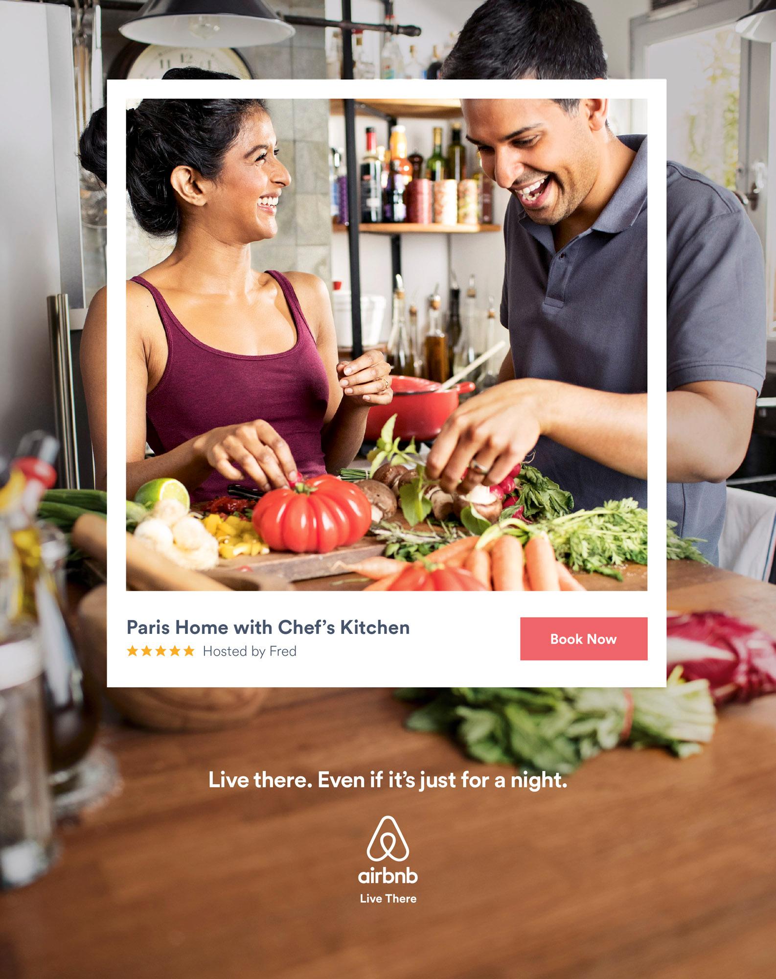 A woman in a purple tank top is cooking in a kitchen with a man, surrounded by various vegetables and cooking utensils.