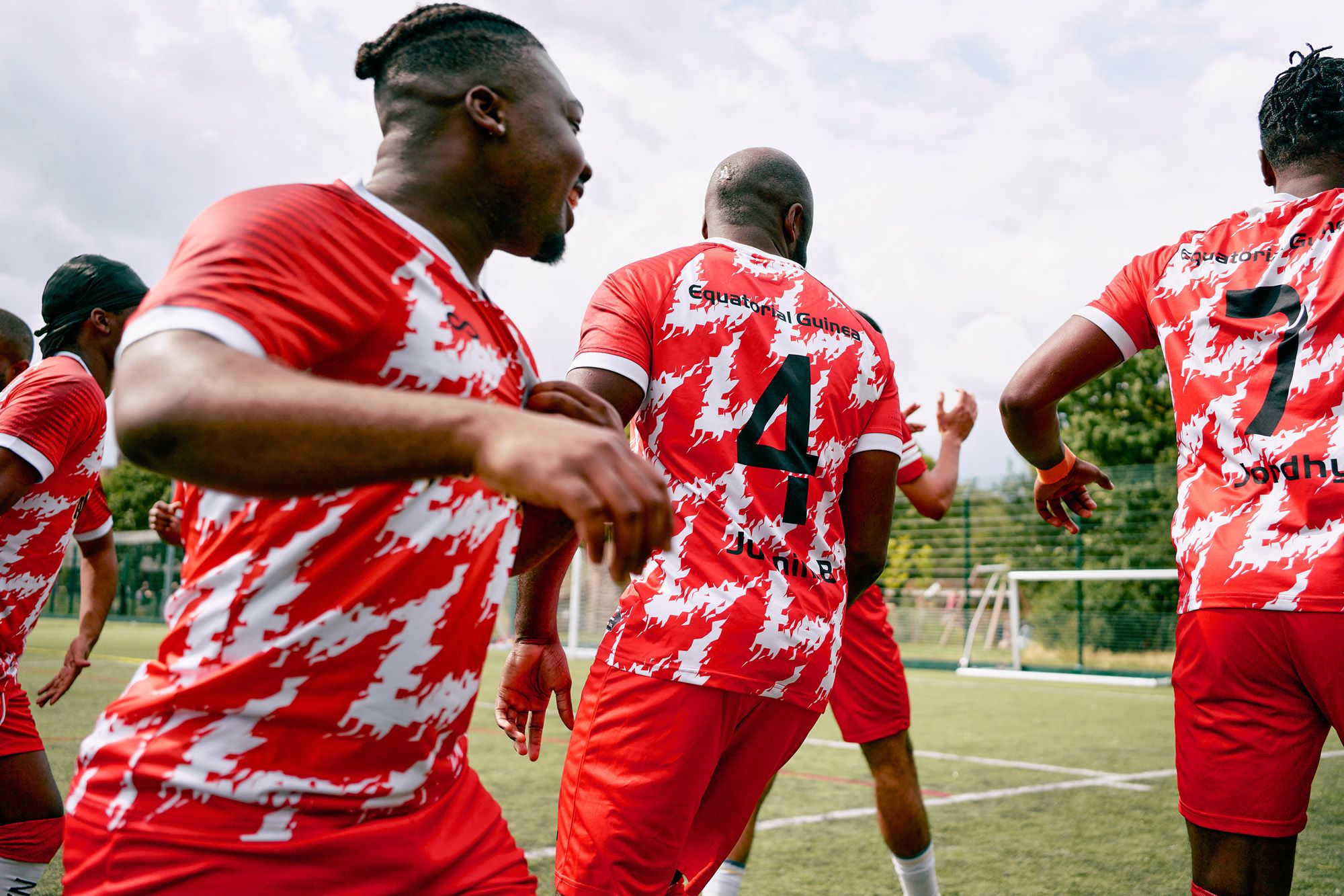A group of football players in red and white jerseys are running on a football field, with a goal in the background.