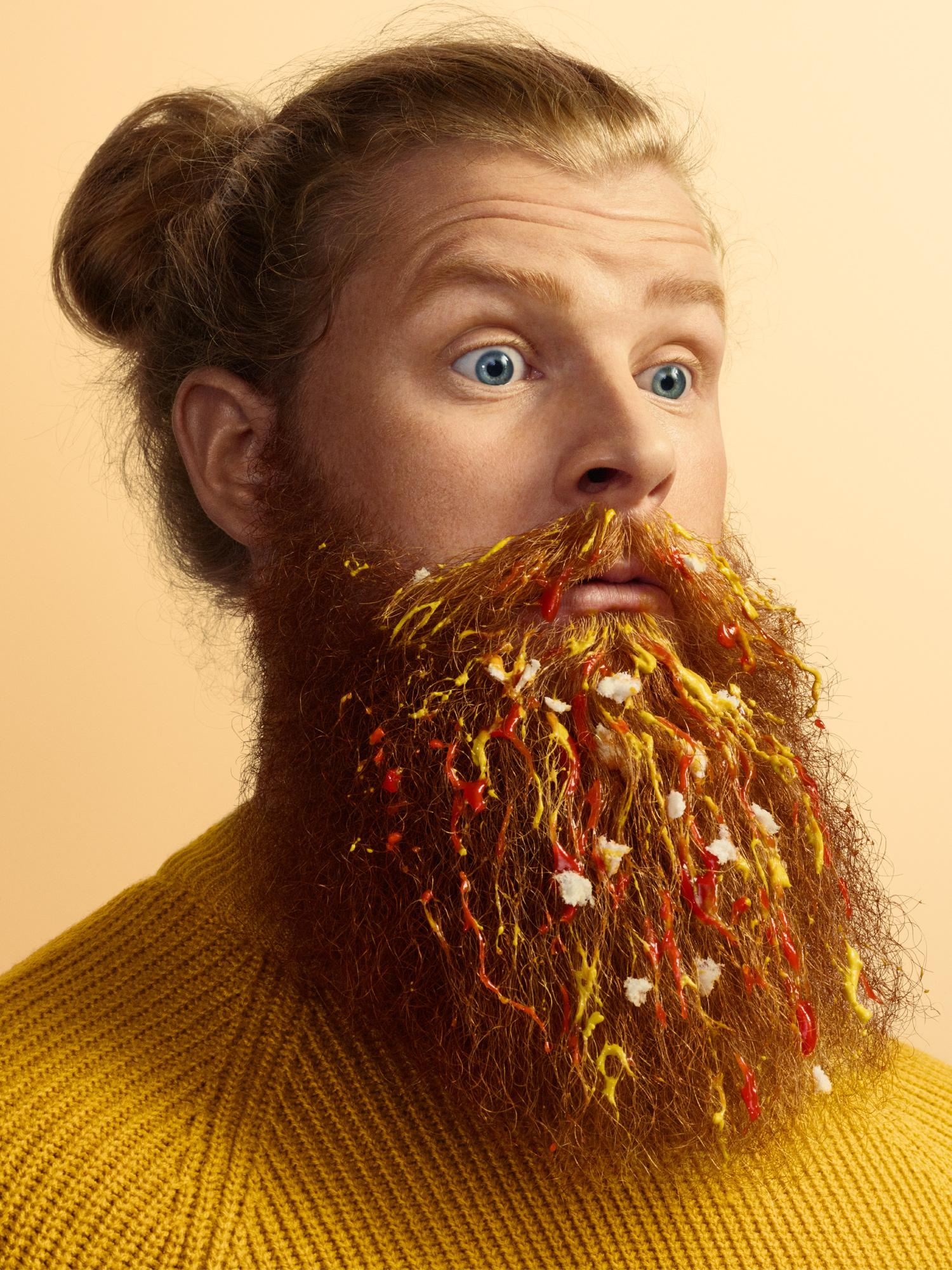 A man with food-stained beard and hair, including ketchup, mustard, and a fried egg.