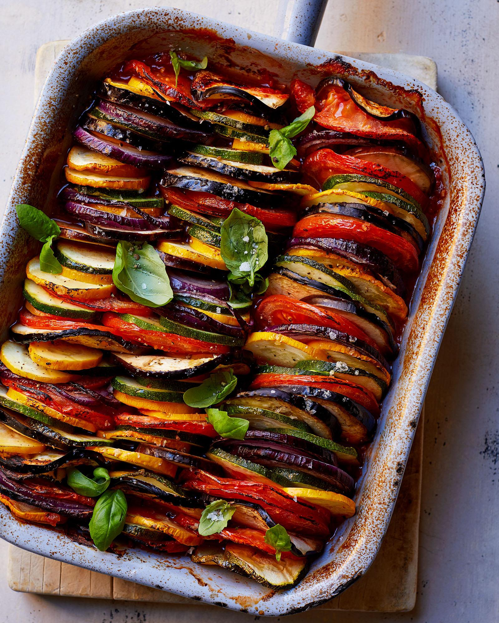 A baking dish filled with a vegetable lasagna, featuring layers of pasta, vegetables, and cheese, topped with a golden brown crust.