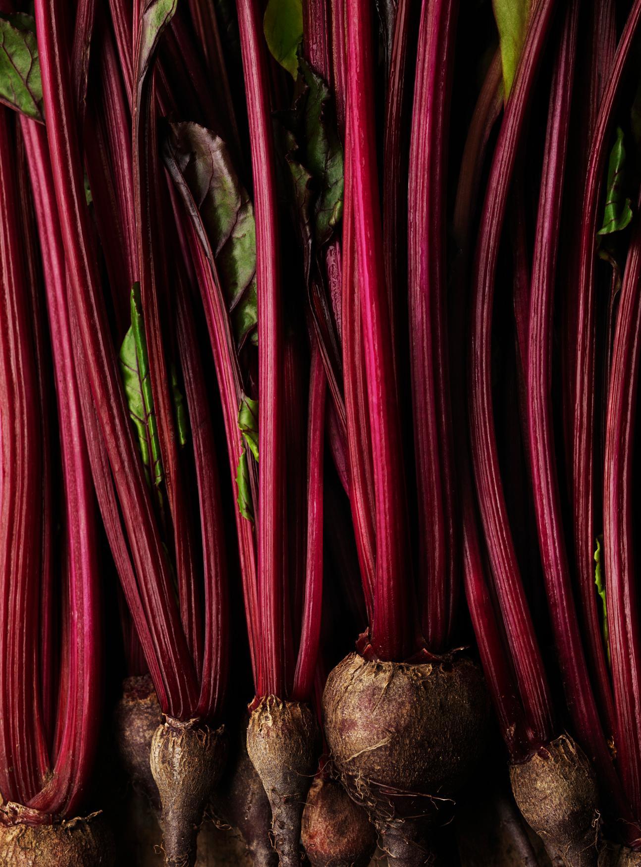 A close-up of a large red beet with green leaves.