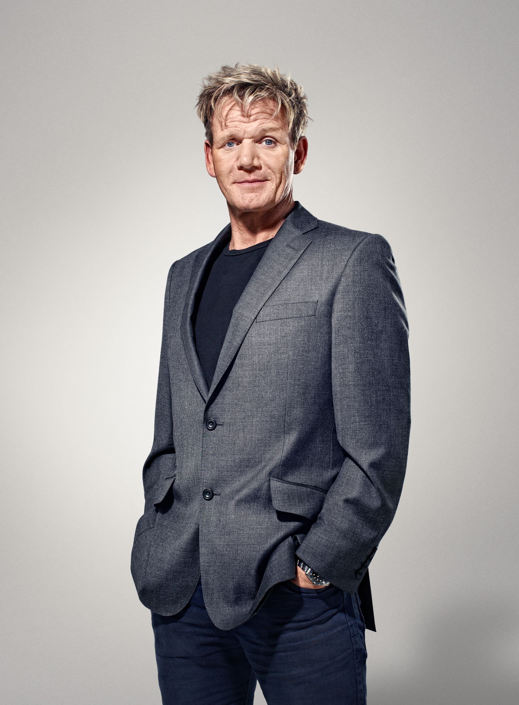 A man in a grey suit and black shirt, with a hint of a smile, looking directly at the camera.