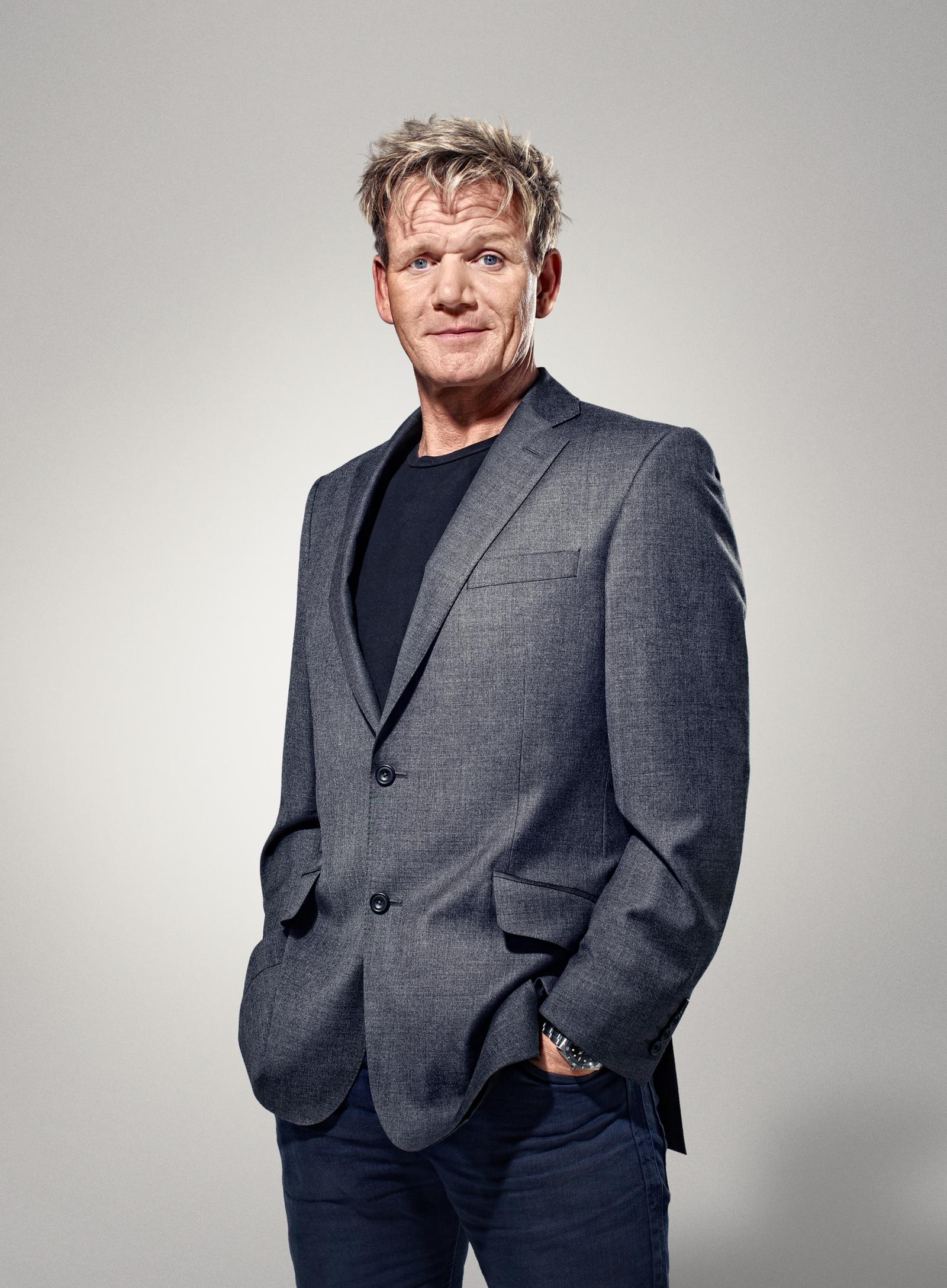A man in a grey suit and black shirt, with a hint of a smile, looking directly at the camera.
