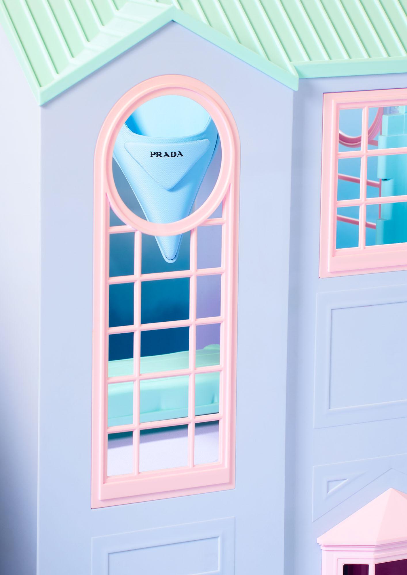 A Prada handbag is visible through a window of a dollhouse.