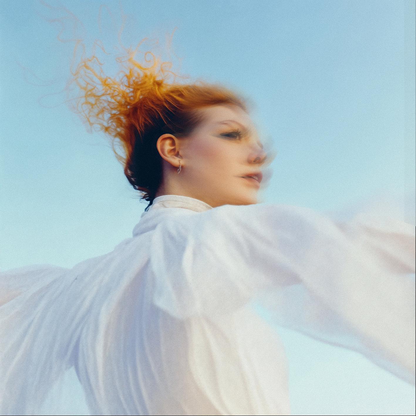 A woman with red hair and a white dress is flying in the air, her dress flowing behind her.