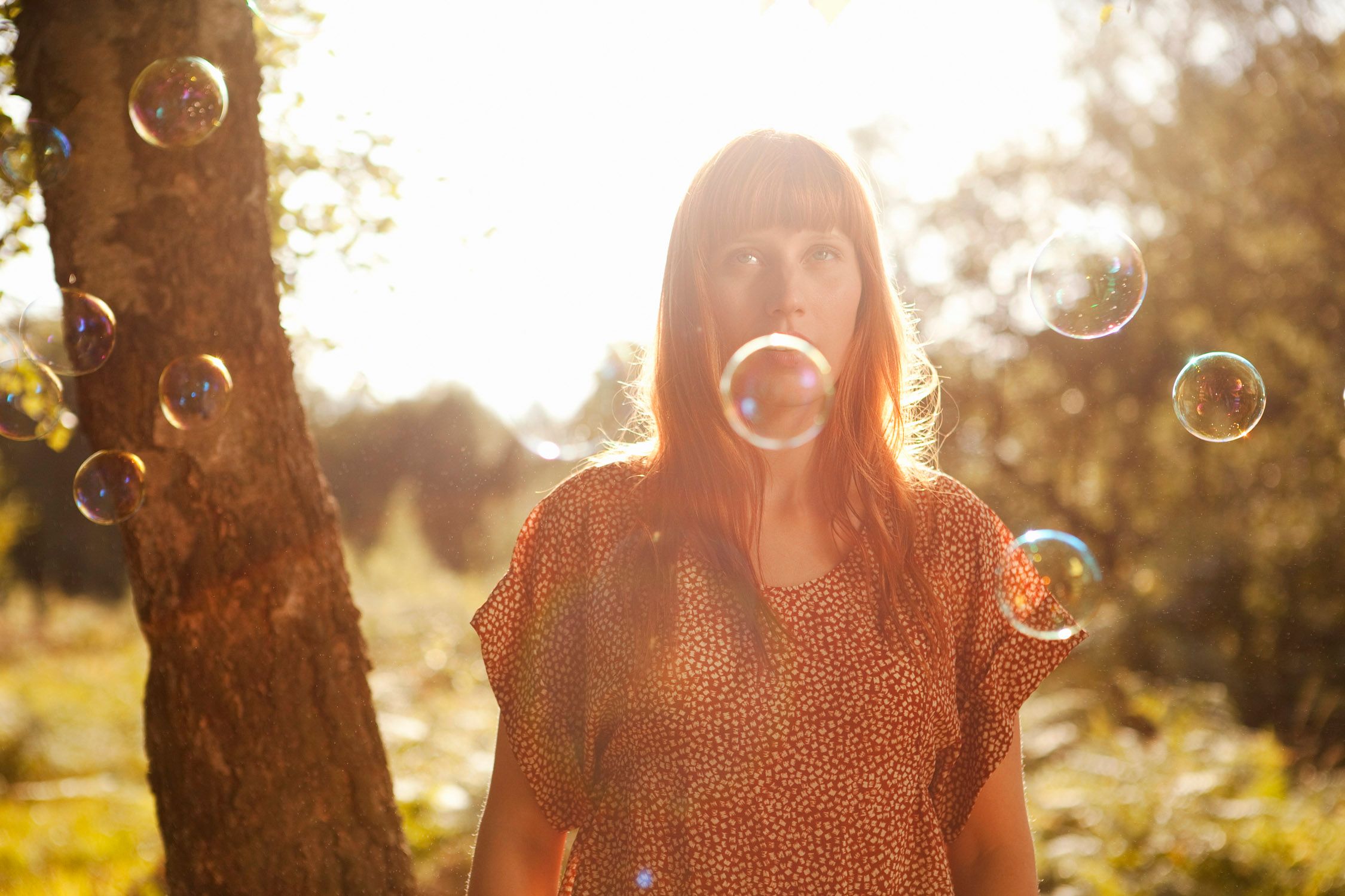 A woman in a red and white polka dot dress stands in a forest with bubbles around her.