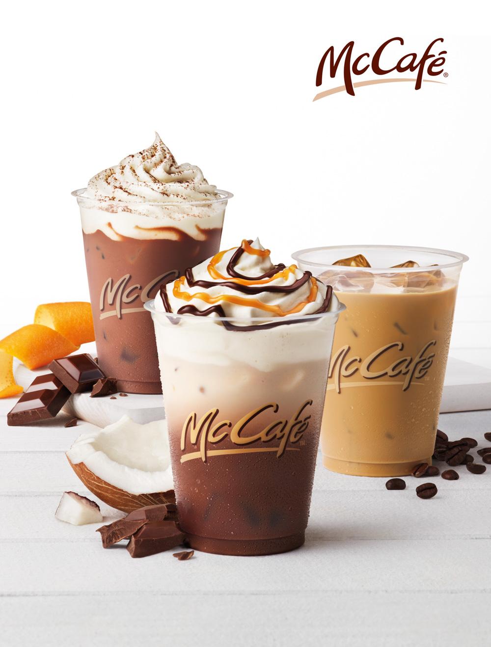 A selection of McCafé drinks, including a Mocha, Cappuccino, and Iced Coffee, with a variety of toppings and a few chocolate and coffee beans in the background.