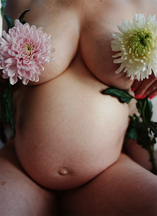 A close-up of a woman holding two large pink and white flowers covering her chest.
