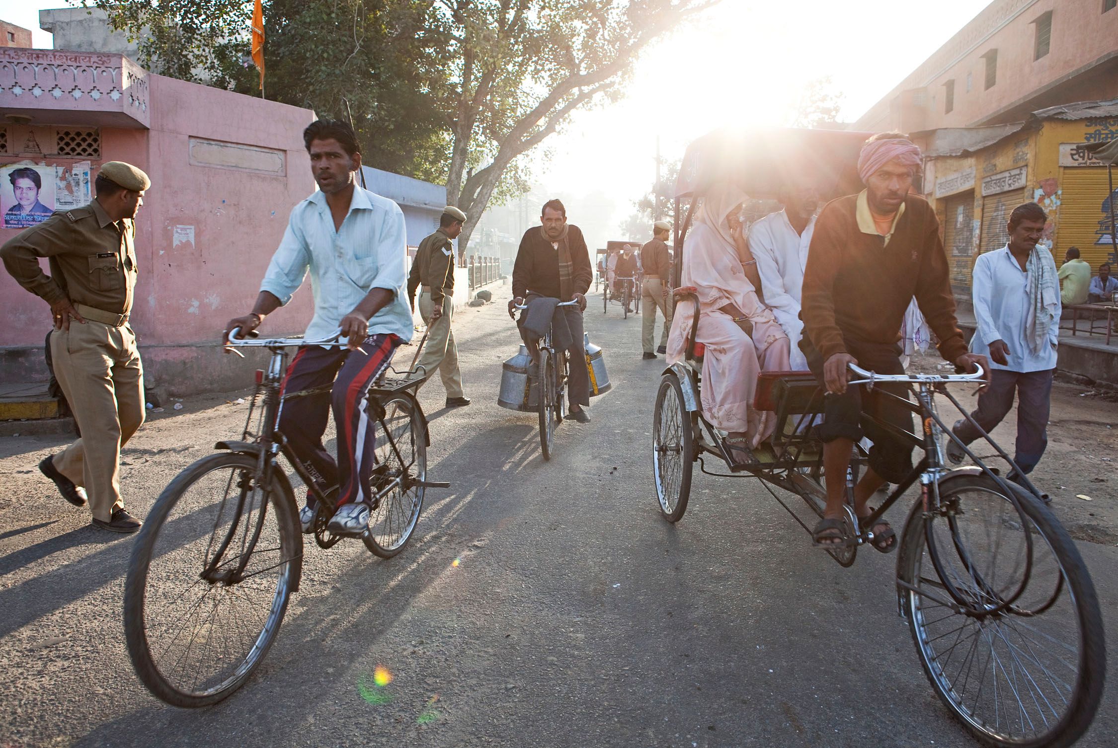 A group of people, including a man in a turban and a woman in a white sari, are riding a rickshaw through a crowded street in a city in India.