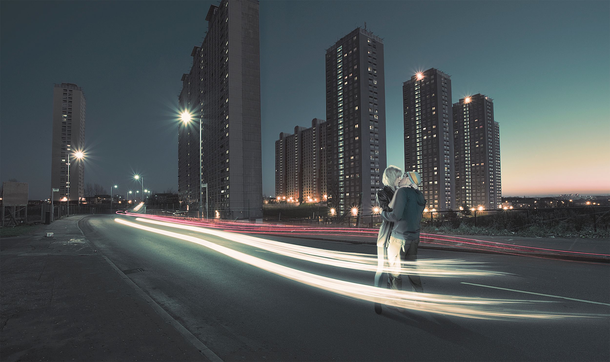 A city street at night with a person in the foreground, looking out at the city skyline.