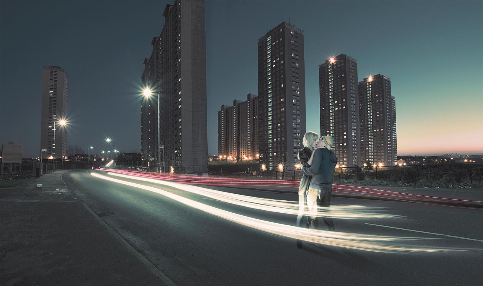 A city street at night with a person in the foreground, looking out at the city skyline.
