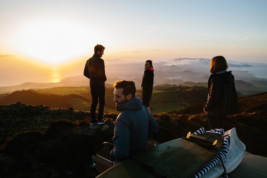 A group of people standing on a mountain peak at sunset, looking out at the landscape.