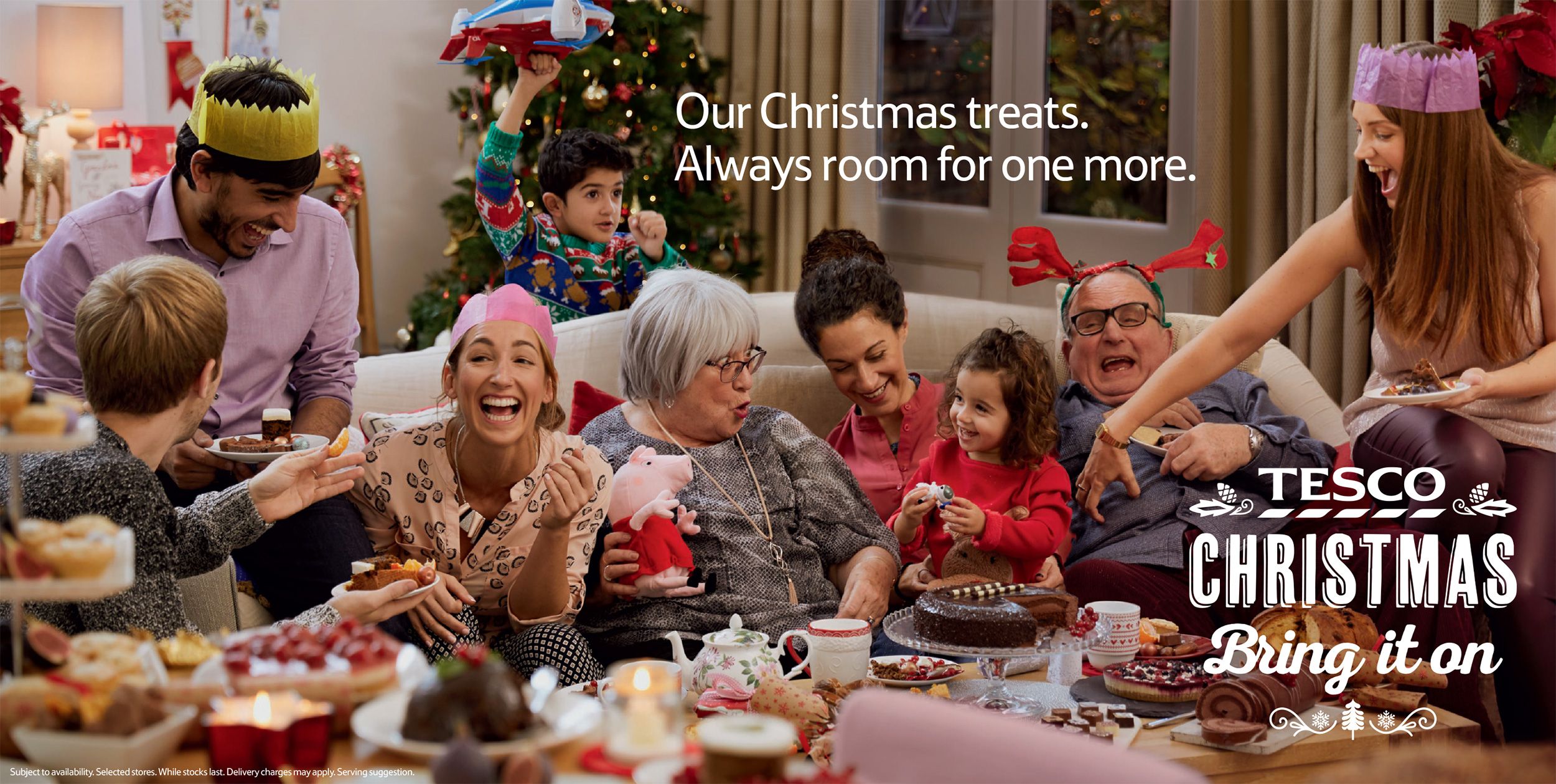 A group of people of all ages, including children, are gathered around a table laden with an assortment of sweet and savory foods, enjoying a festive holiday meal together.