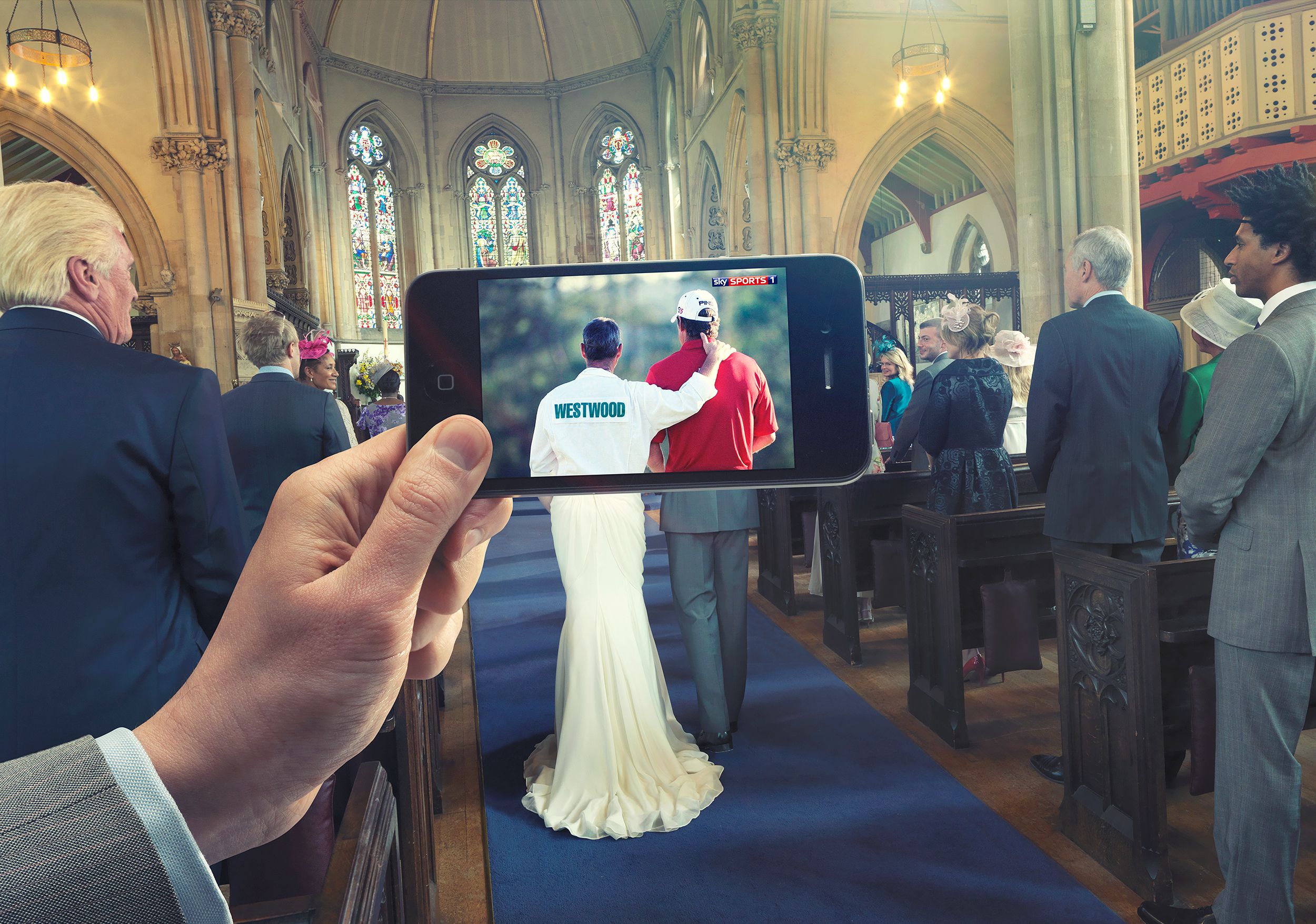 A person holds a smartphone near a church with a TV screen behind showing a sports event.