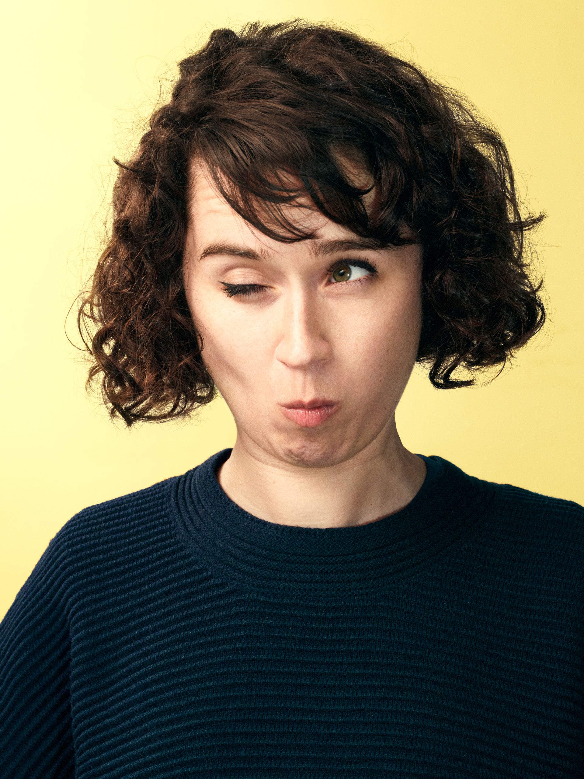 A woman with curly brown hair and a navy blue striped sweater looking directly at the camera with a neutral expression.