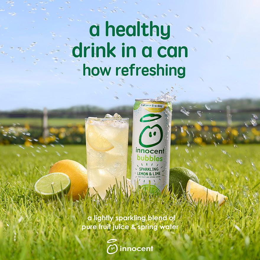 A can of 'Innocent' lemon and lime-flavored sparkling drink, surrounded by lemons and limes, in a grassy field.