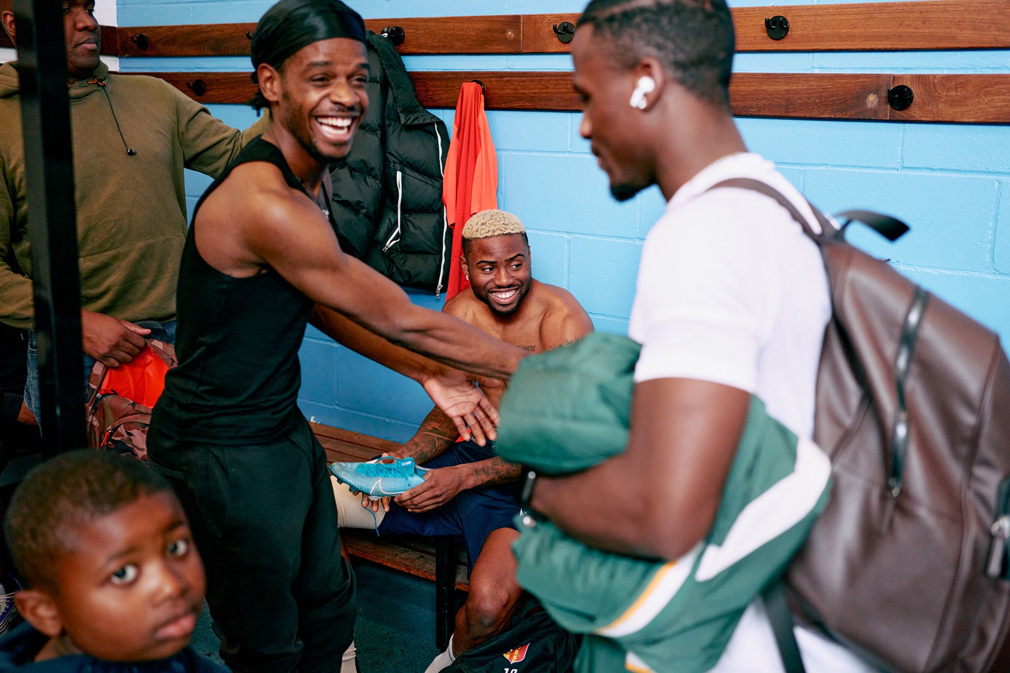 A group of people in a locker room, some holding sports equipment and others sitting on benches.