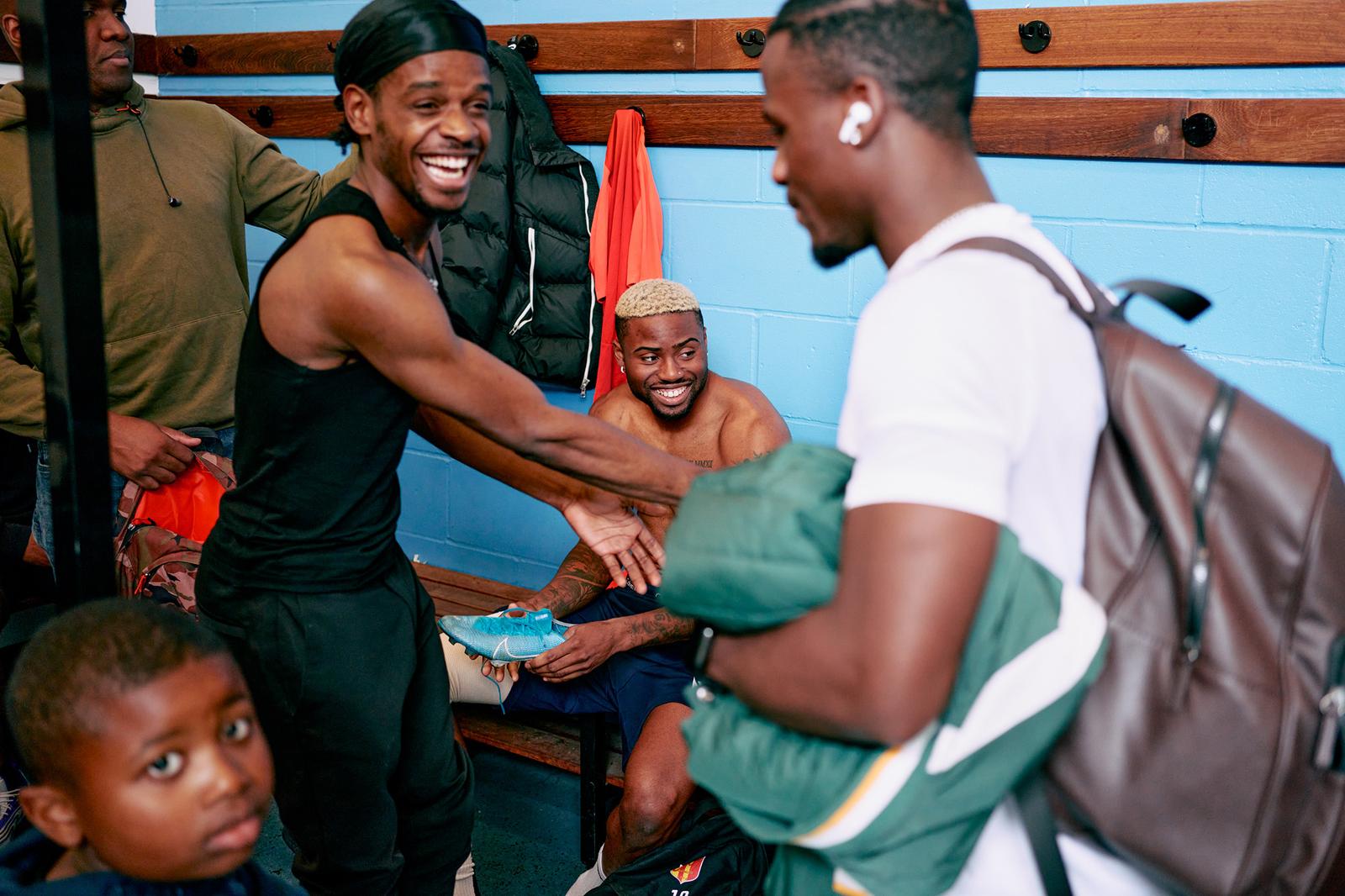 A group of people in a locker room, some holding sports equipment and others sitting on benches.