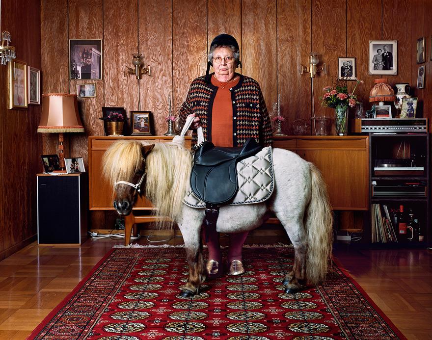 An elderly woman stands next to a miniature horse in a living room.