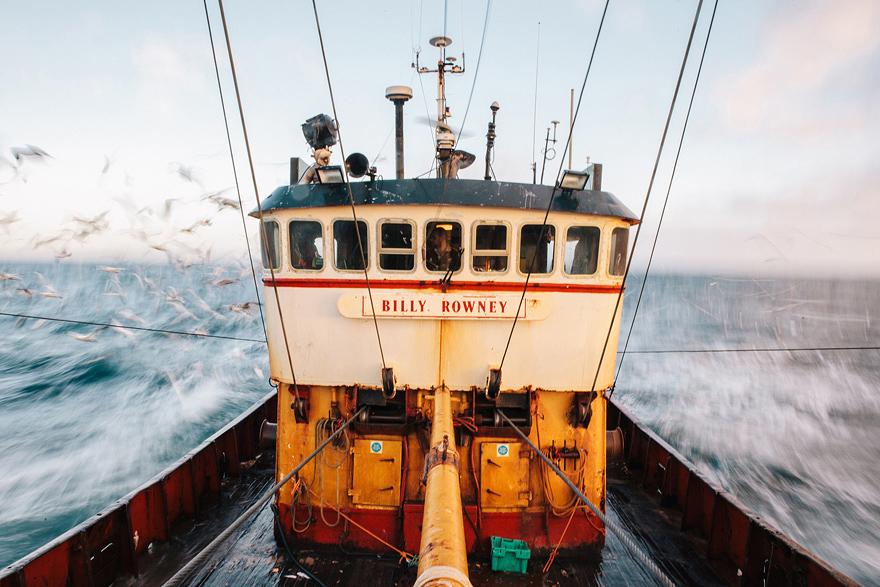 A large fishing boat, the Billy Rowney, is sailing through the ocean, with seagulls flying overhead.