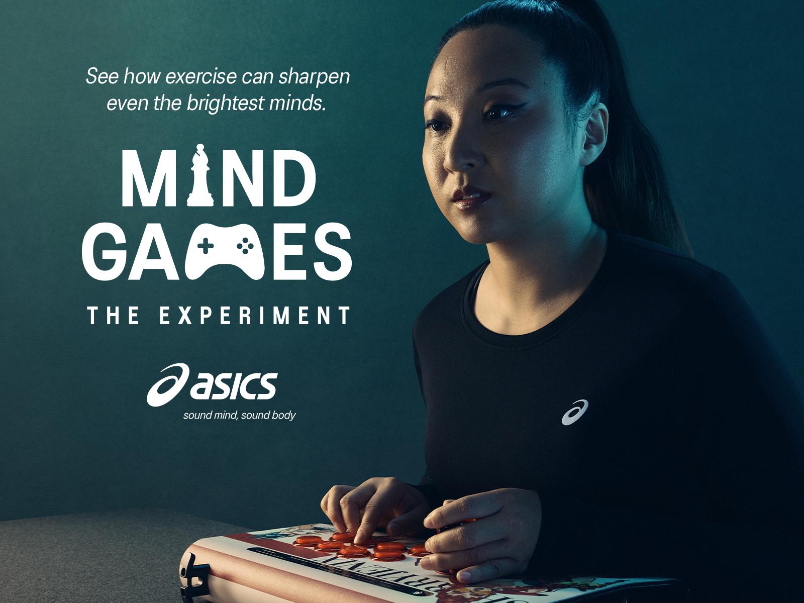 A woman in a black t-shirt with the ASICS logo, sitting at a table with a gaming console and a controller.