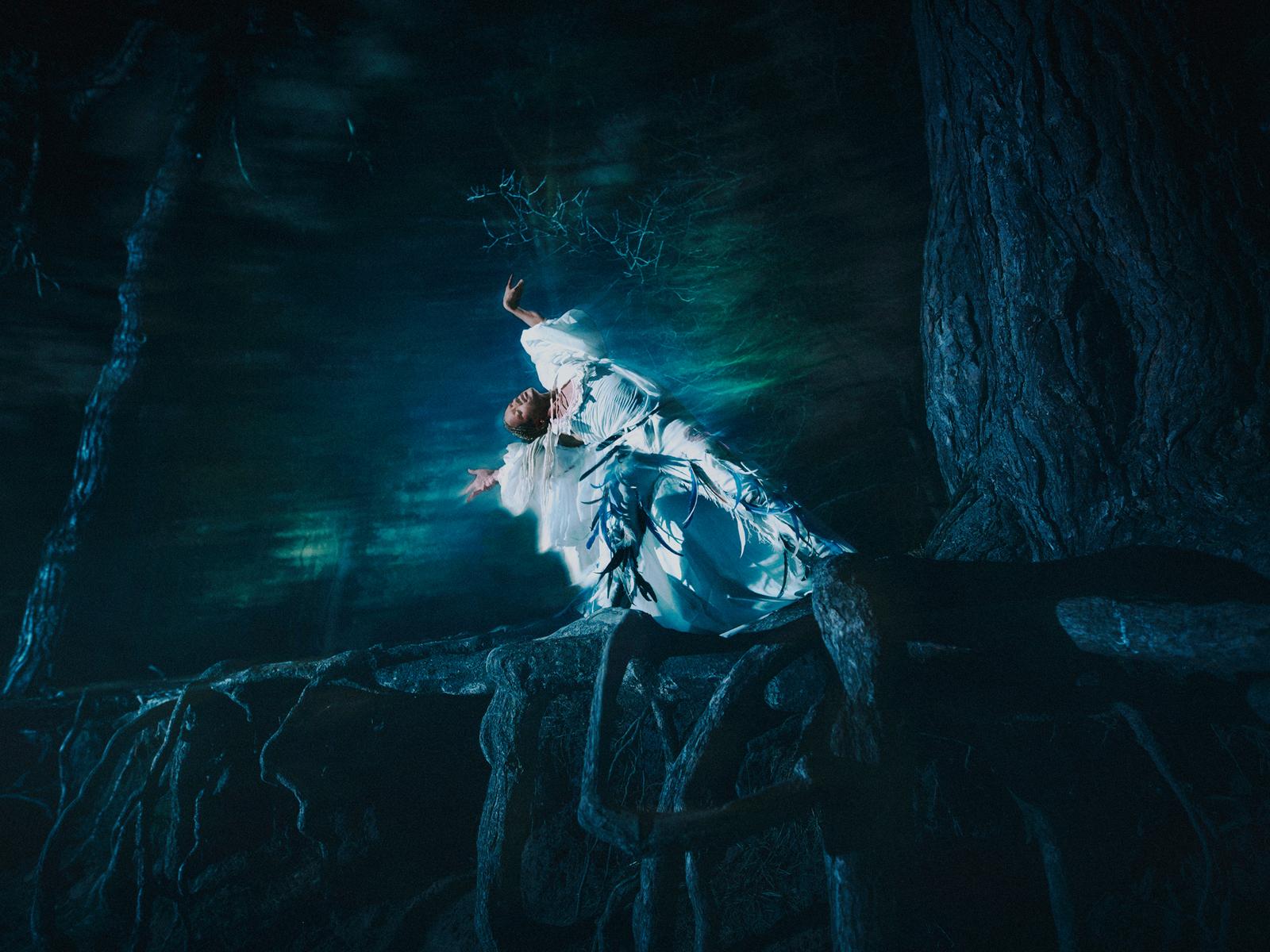 A woman stands on rocks, arms outstretched, head thrown back.